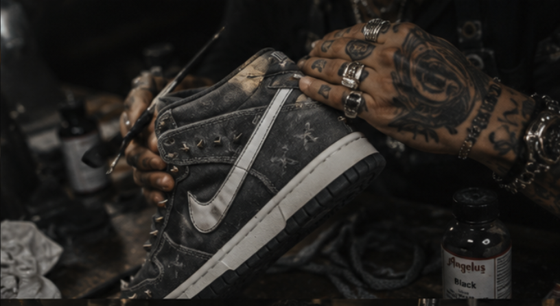 Tattooed hands hand-finishing a studded Nike high-top at the workbench
