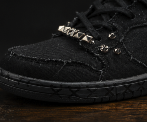 Macro of pyramid studs and raw frayed seams across the toe of the black high-top