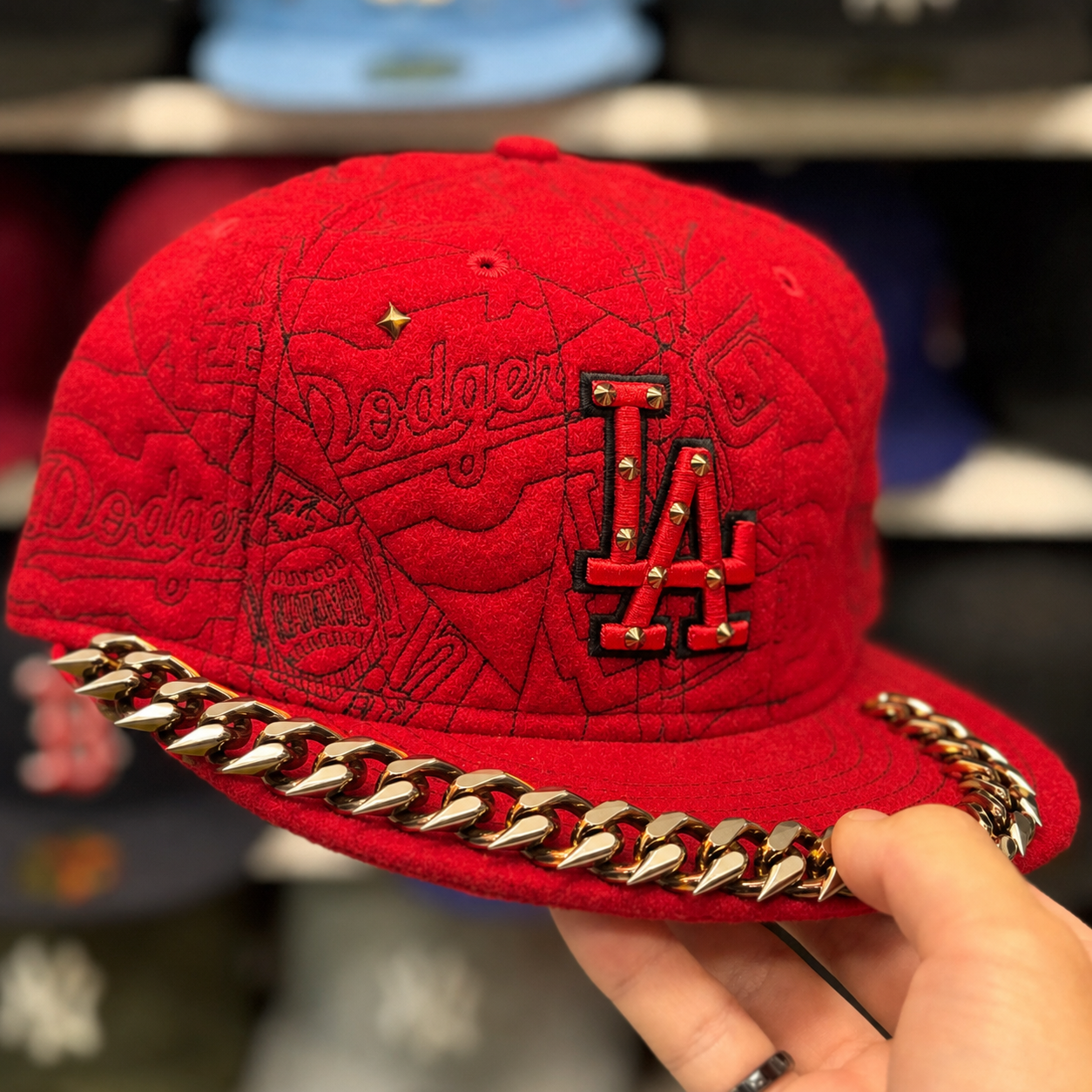 Red wool cap with a gold spiked Cuban-link chain across the brim and a studded LA mark