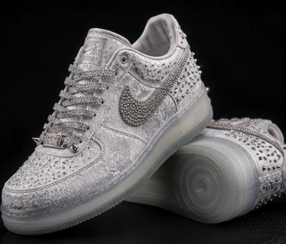 Pair of white embossed low-top footwear objects covered in silver spikes with a crystal-set swoosh and translucent sole